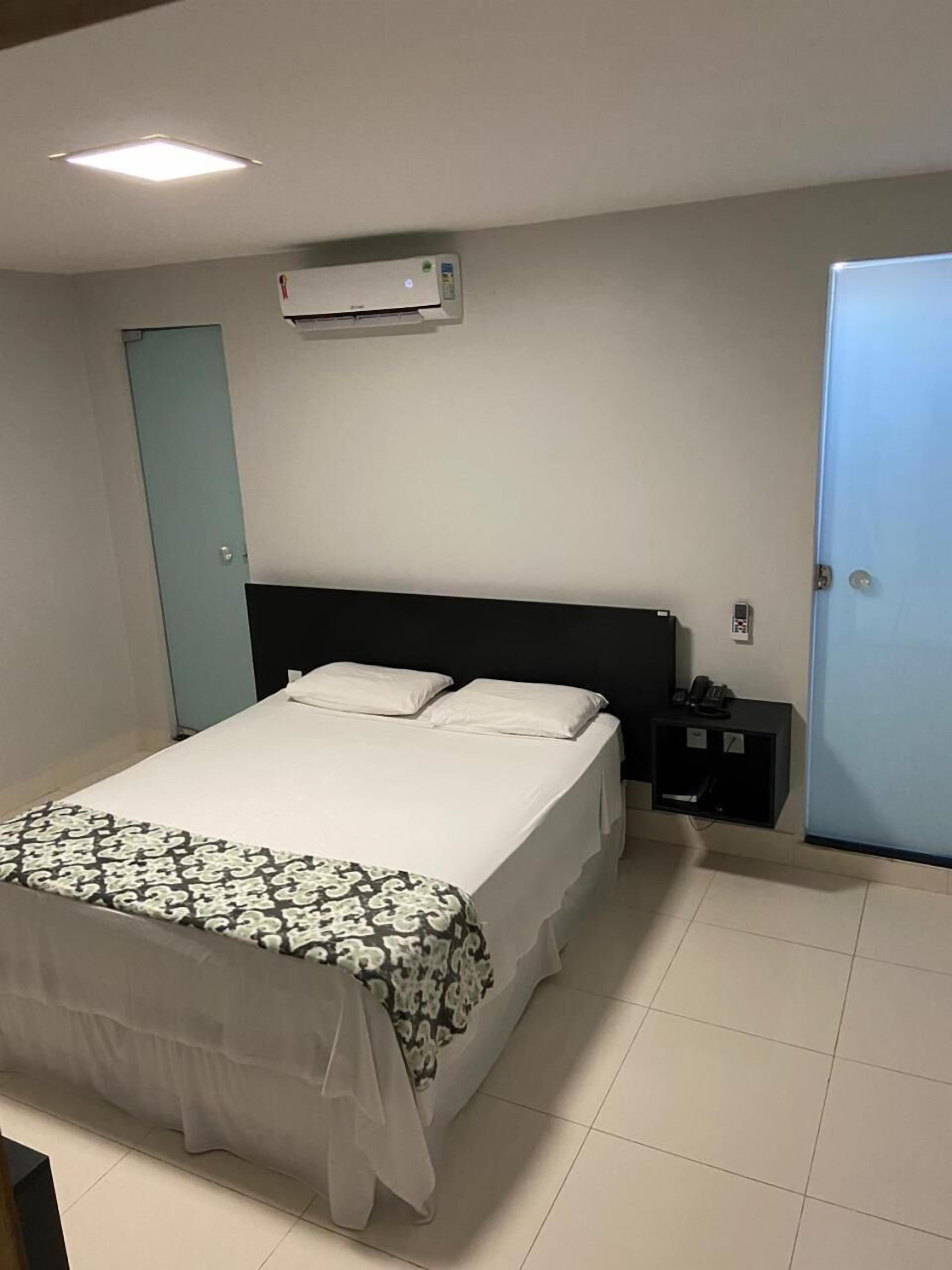 A hotel room with a bed, bedside table, and a door.