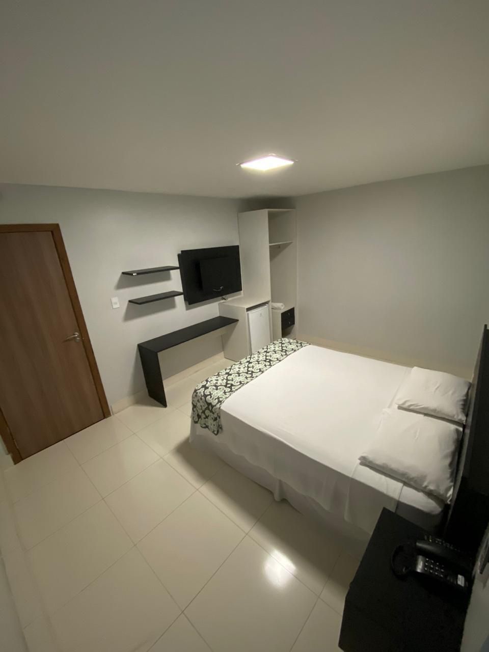 A hotel room with a bed, a television mounted on the wall, a small desk, and a door.