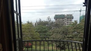 Un balcon ouvert avec une table ronde et quatre chaises, un sol carrelé et une vue sur des bâtiments et des arbres en arrière-plan.