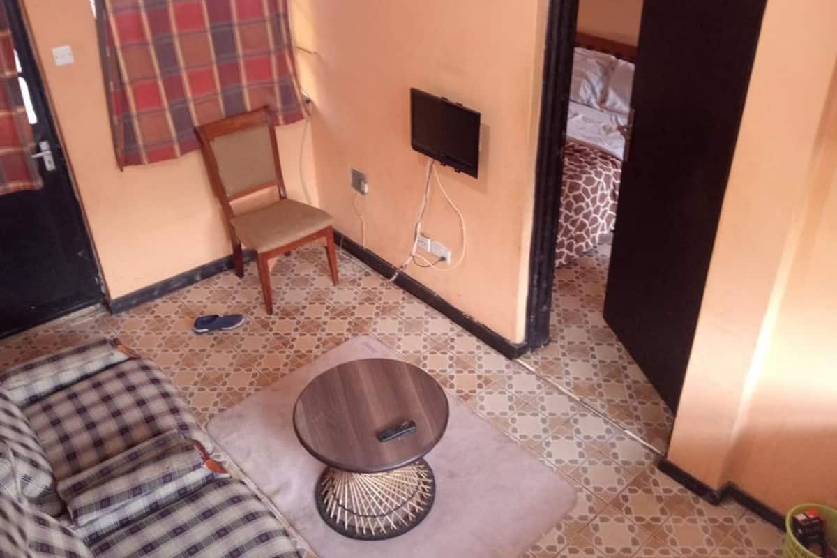 A small room with a sofa, a chair, a small table, a television, and a bed with patterned bedding.