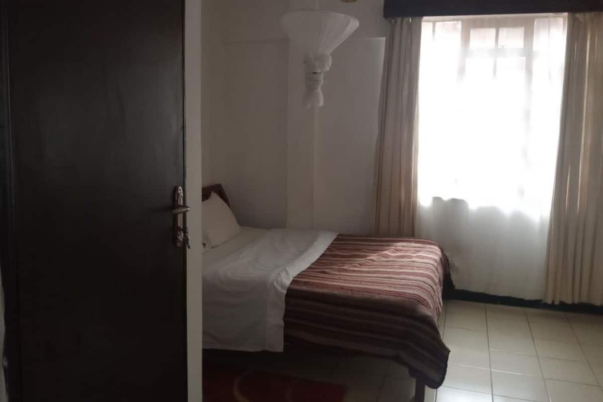 A bedroom with a bed, a window with curtains, and a hanging light fixture.