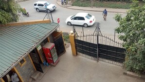 Une entrée fermée par un portail en métal, un réfrigérateur Coca-Cola et un bâtiment doté d’un toit végétalisé.