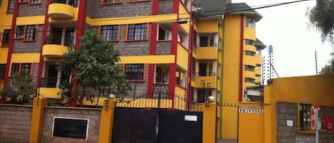 Un immeuble à plusieurs étages aux façades extérieures jaunes et rouges, doté de balcons et d’une entrée fermée par un portail.