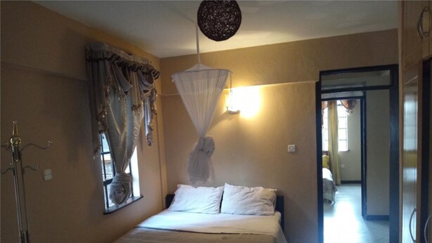 Une chambre à coucher avec un lit, une fenêtre avec des rideaux, un luminaire suspendu et une porte donnant sur une autre pièce.
