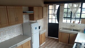Une cuisine avec des meubles de rangement en bois, un réfrigérateur blanc, un four à micro-ondes et une fenêtre avec des rideaux.