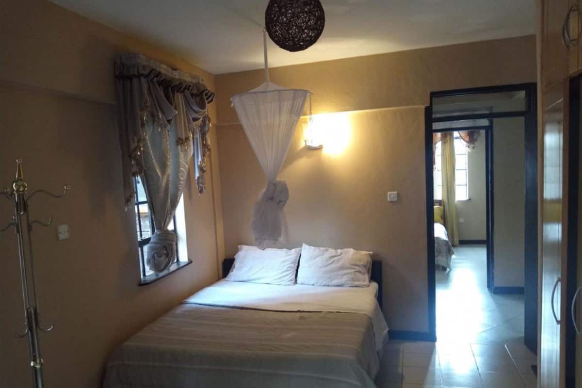 A bedroom with a bed, a canopy, a window with curtains, a floor lamp, and a door leading to another room.