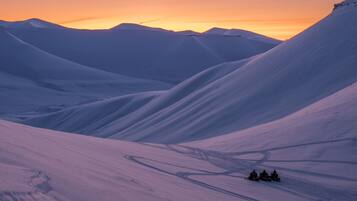 Paisaje nevado con terreno ondulado y un grupo de personas en motos de nieve.