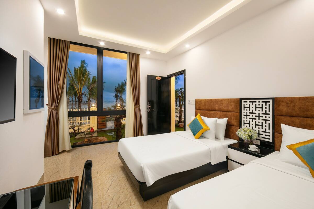 A hotel room with two beds, a TV, a balcony with a view, and a door leading outside.
