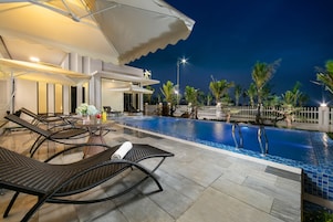 A pool area with lounge chairs and umbrellas, surrounded by palm trees and a white fence.