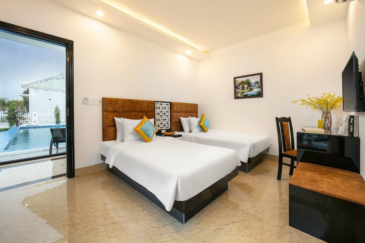 A hotel room with two beds, a desk, a chair, and a view of a swimming pool.