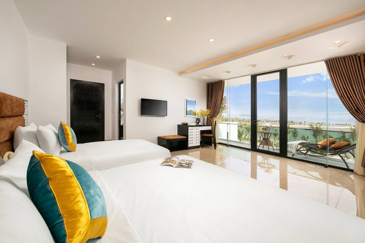 A hotel room with a large bed, a desk, a TV, and a balcony with a view.