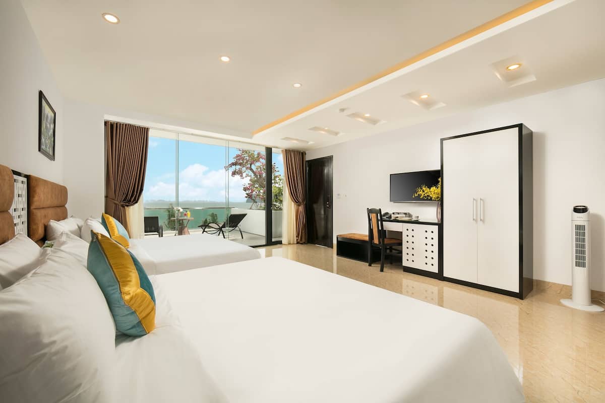 A hotel room with two beds, a desk, a TV, and a balcony with a view.