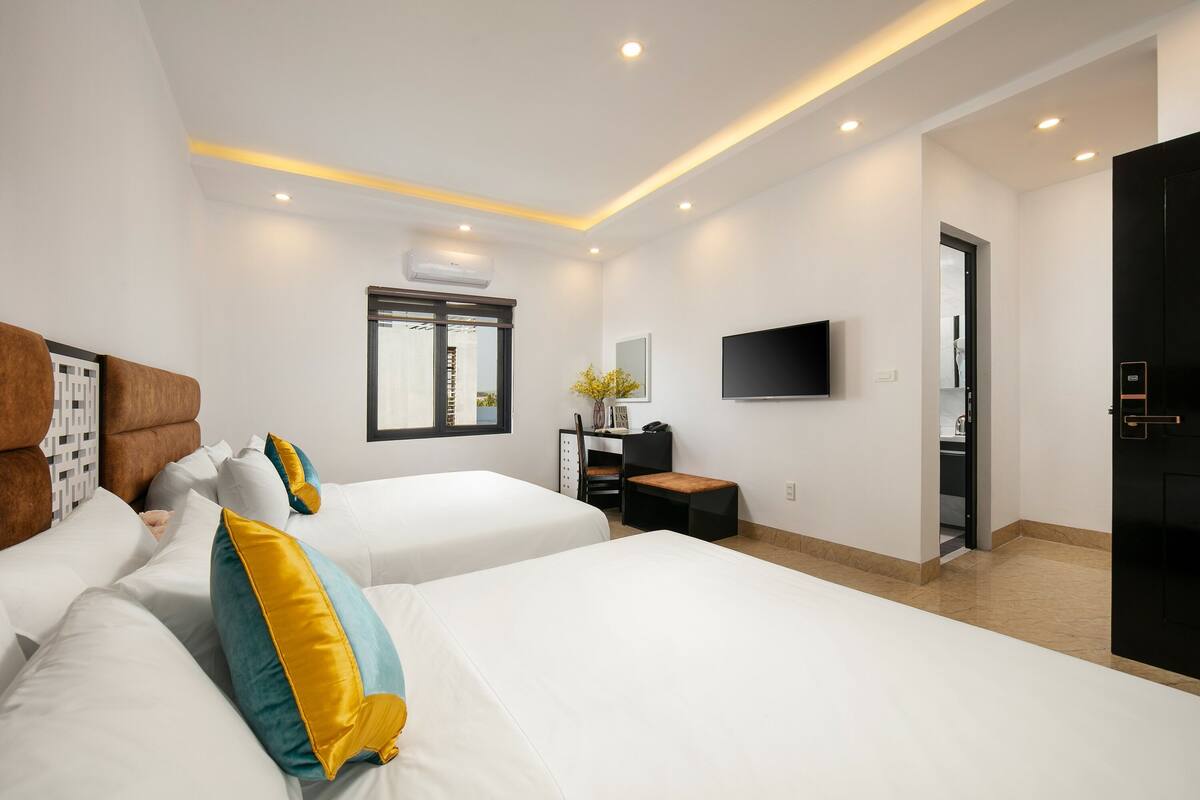 A modern hotel room with two beds, a desk, a chair, a TV, and a wardrobe.