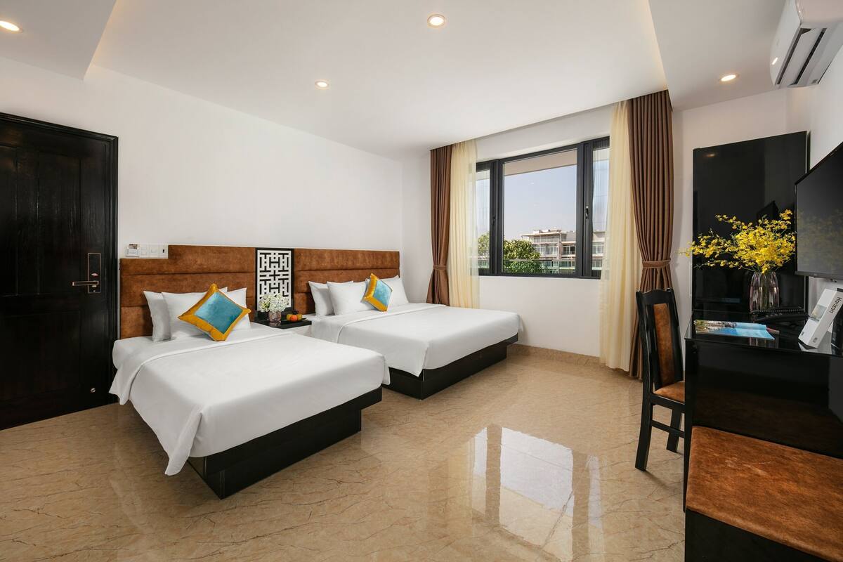 A hotel room with two beds, a television, a desk, and a window with curtains.