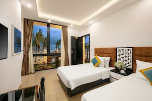 A hotel room with two beds, a TV, and a balcony with a view of palm trees.