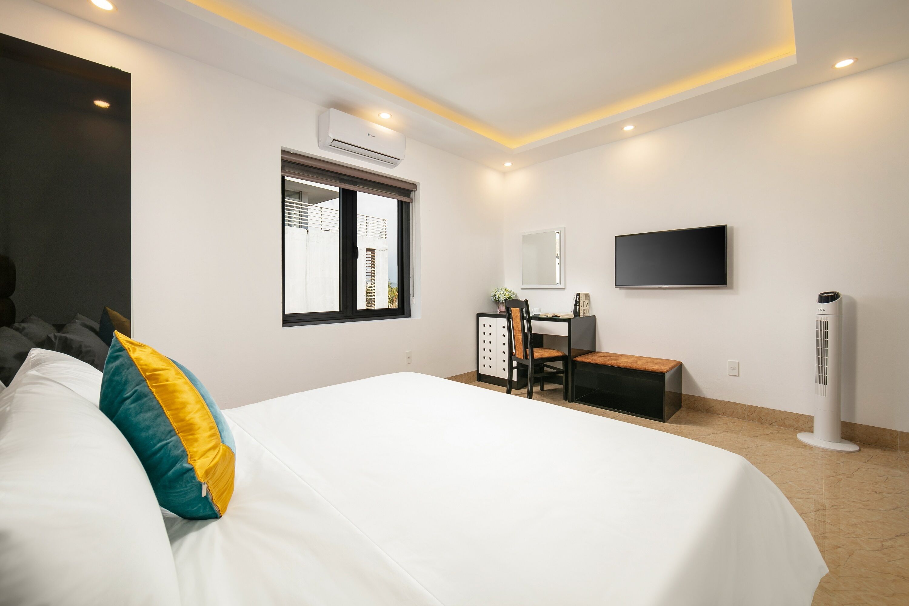 A modern hotel room with a large bed, a desk, a chair, a flat-screen TV, and an air conditioning unit.
