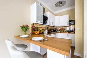 Een moderne keuken met witte kasten, een houten aanrecht en een eethoek met twee witte stoelen.