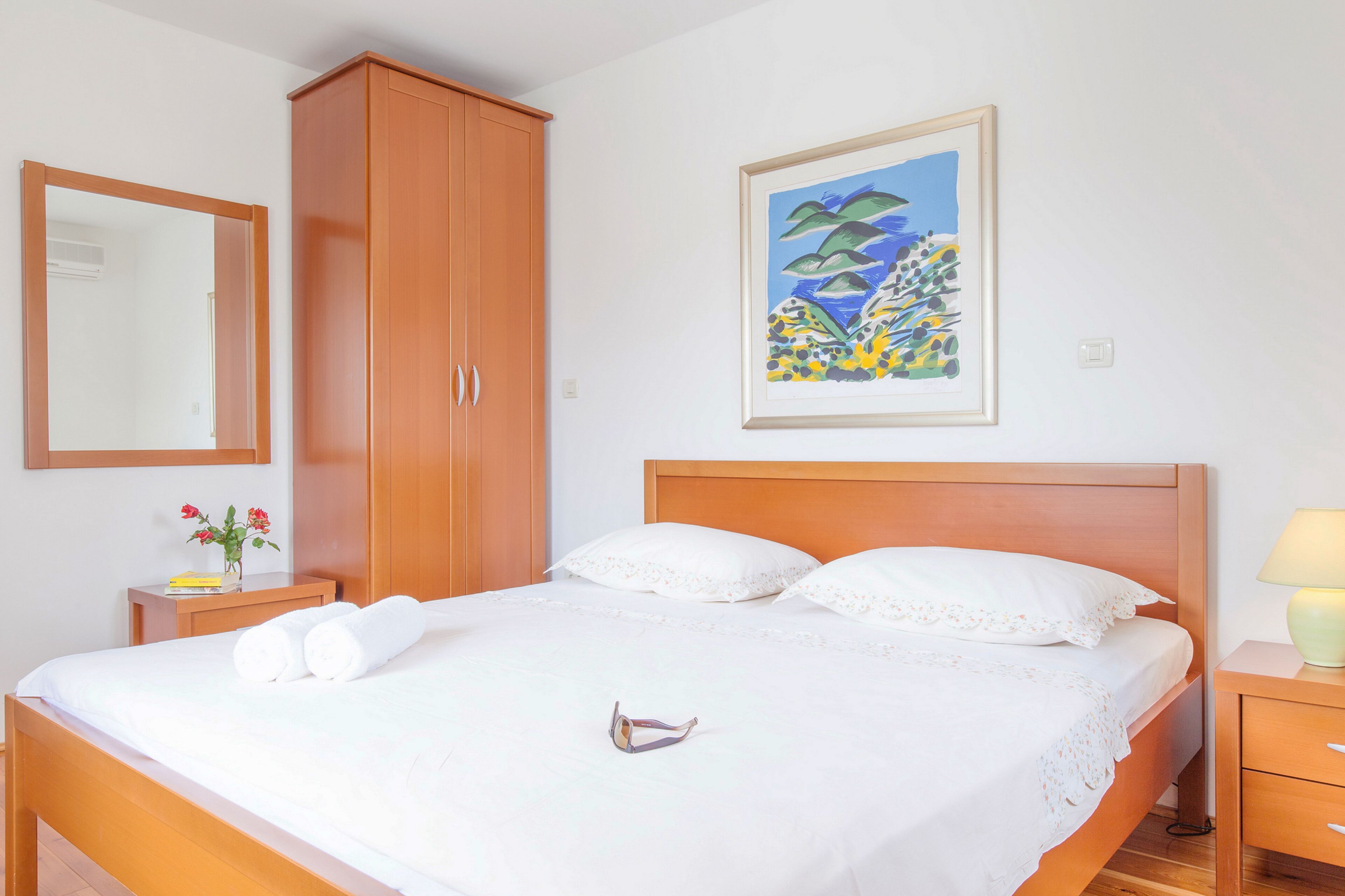 A neatly made bed with white linens, a wooden headboard, and a pair of sunglasses on the bed.