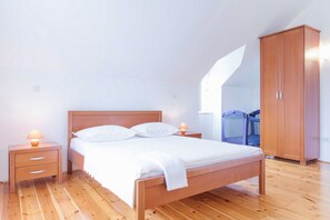 Une chambre à coucher avec un lit en bois, des tables de chevet, une armoire et une fenêtre donnant sur un balcon.