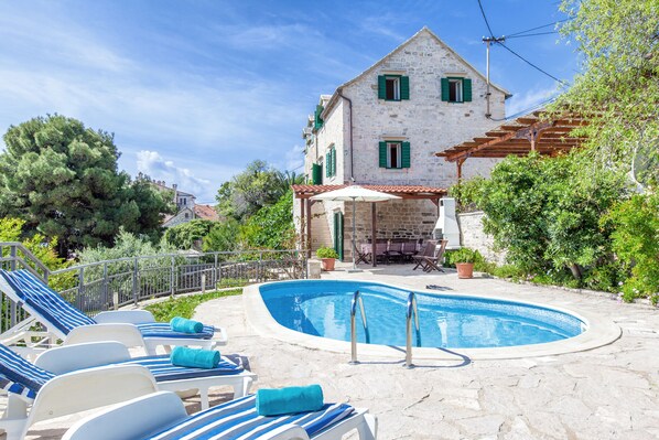 Un bâtiment en pierre doté d’une piscine, de chaises longues et d’une pergola.