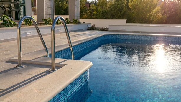 A swimming pool with metal ladders and a tiled edge, surrounded by a stone wall and greenery. - Villa Makarac (Milna)