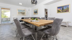 A modern dining area with a wooden table, grey upholstered chairs, and a hanging light fixture. - Villa Makarac (Milna)