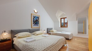 A modern bedroom with a large bed, two smaller beds, wooden flooring, a painting on the wall, and a window with a view. - Villa Dubrava (Pucisca)
