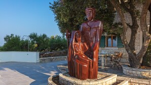 A bronze statue of a seated woman and a standing man in a landscaped outdoor area with a building in the background. - Villa Dubrava (Pucisca)