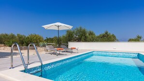 A swimming pool with a clear blue water, surrounded by a white wall and a metal ladder. There are two lounge chairs and an umbrella. - Villa Dubrava (Pucisca)