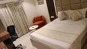 Hotellihuone, jossa on suuri sänky, työpöytä tuolilla, pieni pyöreä pöytä ja sohva.