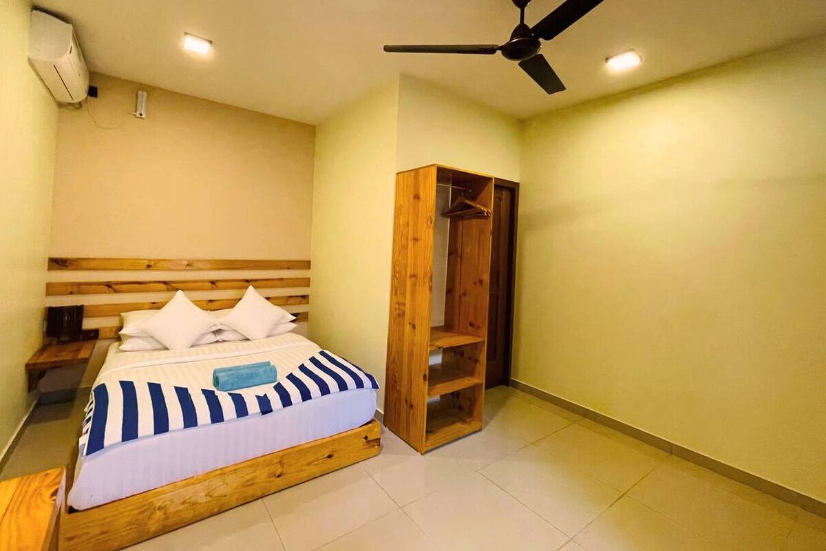 A bedroom with a bed, a wooden wardrobe, a ceiling fan, and an air conditioning unit.