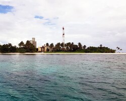 A coastal view with a clear sky, a sandy beach, palm trees, and a building with a tower.