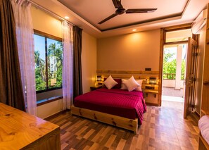 Quarto com cama grande, cabeceira de madeira e vista para palmeiras pela janela.