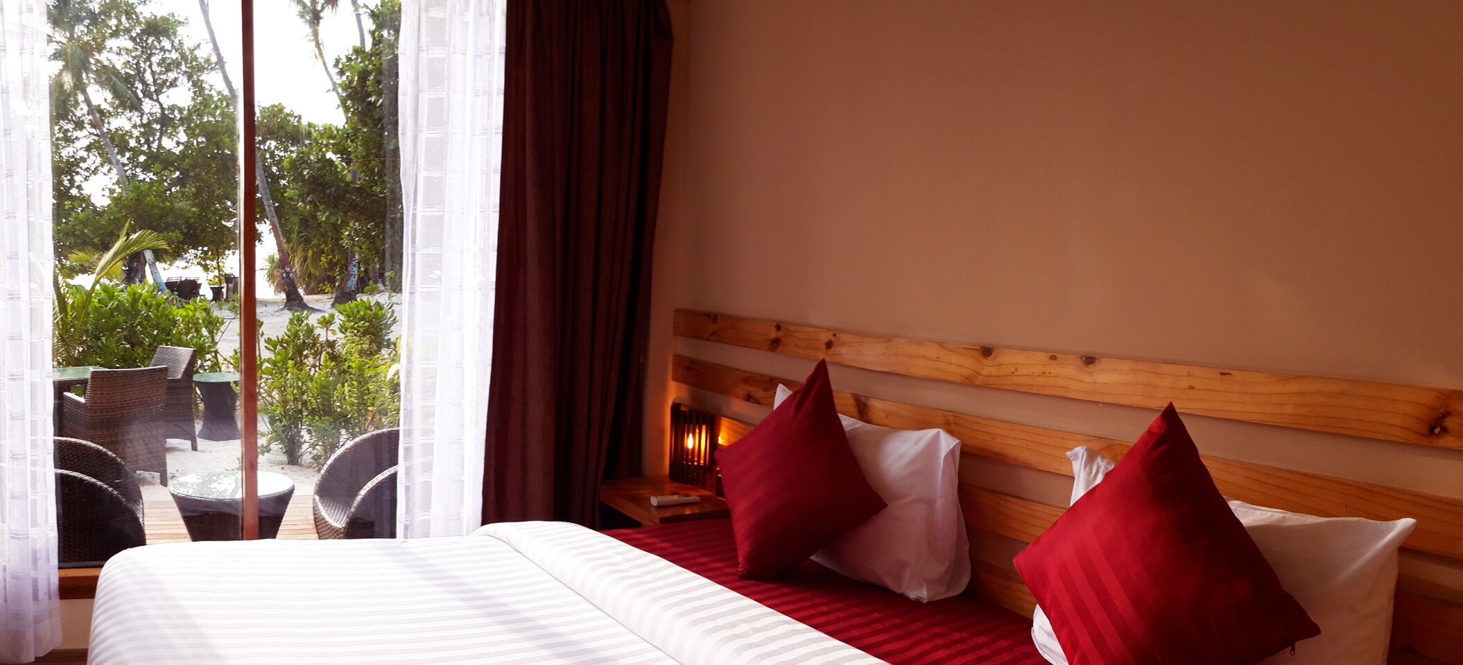 A hotel room with a large bed, wooden headboard, and a view of outdoor seating and greenery.