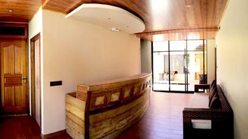 A reception area with a wooden reception desk, a wooden door, and a view of the outside through large glass doors.