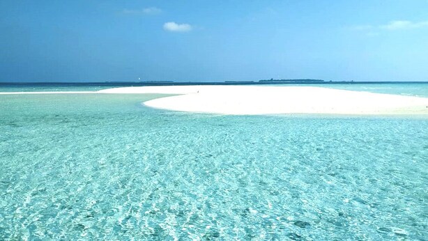 Una spiaggia con acque cristalline turchesi e una distesa di sabbia bianca.
