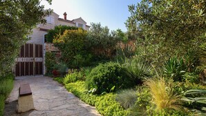 A stone pathway leading to a house with a gated entrance, surrounded by lush greenery and various plants. - Villa Lukrecia (Supetar)