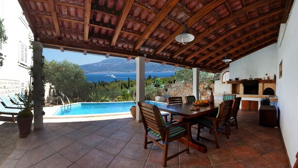 A covered outdoor area with a pool, dining table, chairs, and a stone wall. - Villa Lukrecia (Supetar)