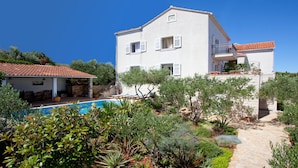 A two-story building with a swimming pool, surrounded by lush greenery and a clear blue sky. - Villa Lukrecia (Supetar)