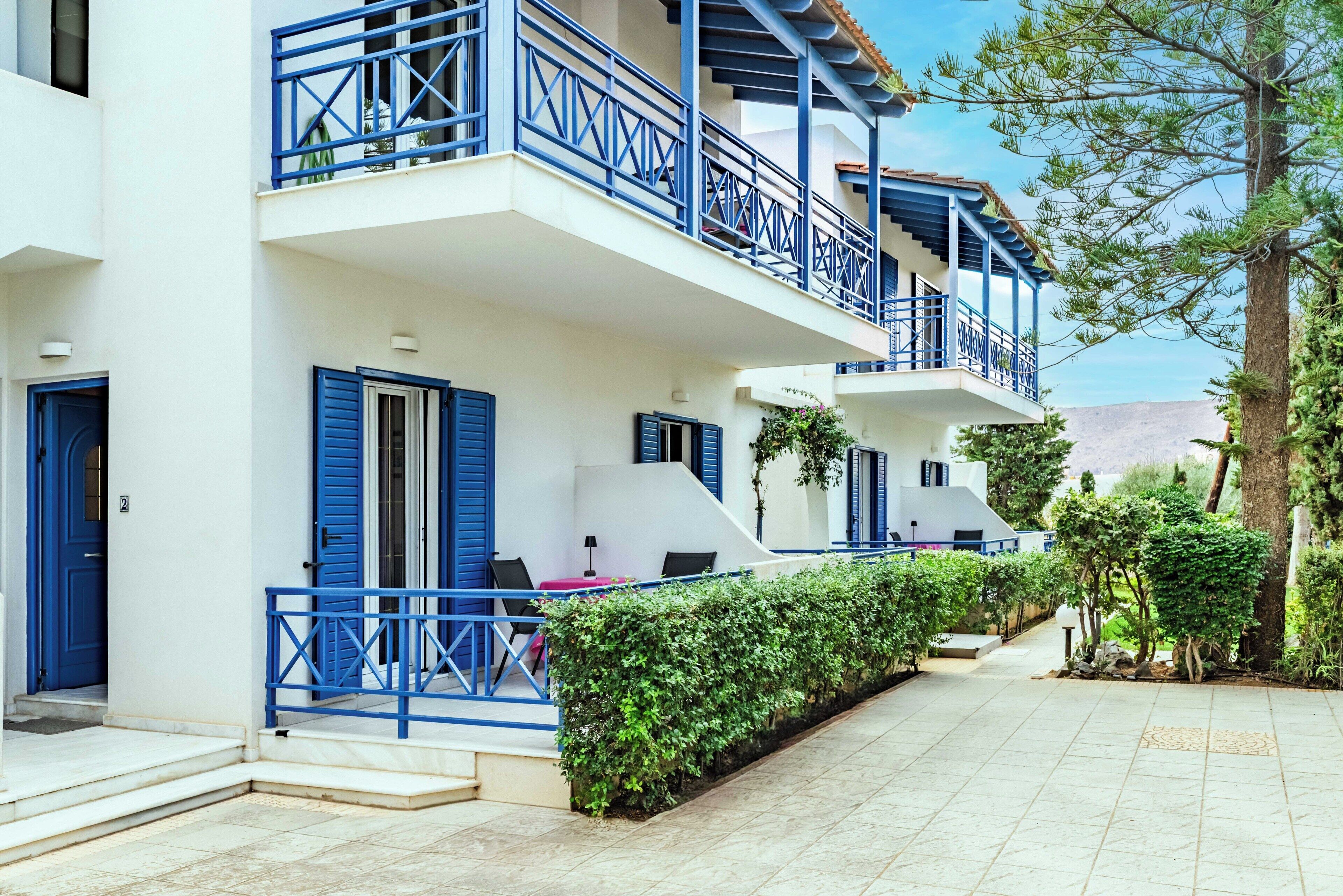 Un edificio de dos pisos con balcones azules, paredes blancas y un patio con azulejos.