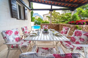 Un espace extérieur abrité où l’on peut prendre ses repas, avec une piscine en arrière-plan.