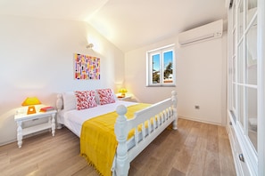 Une chambre à coucher comprenant un lit, des tables de chevet, une fenêtre et un climatiseur fixé au mur.