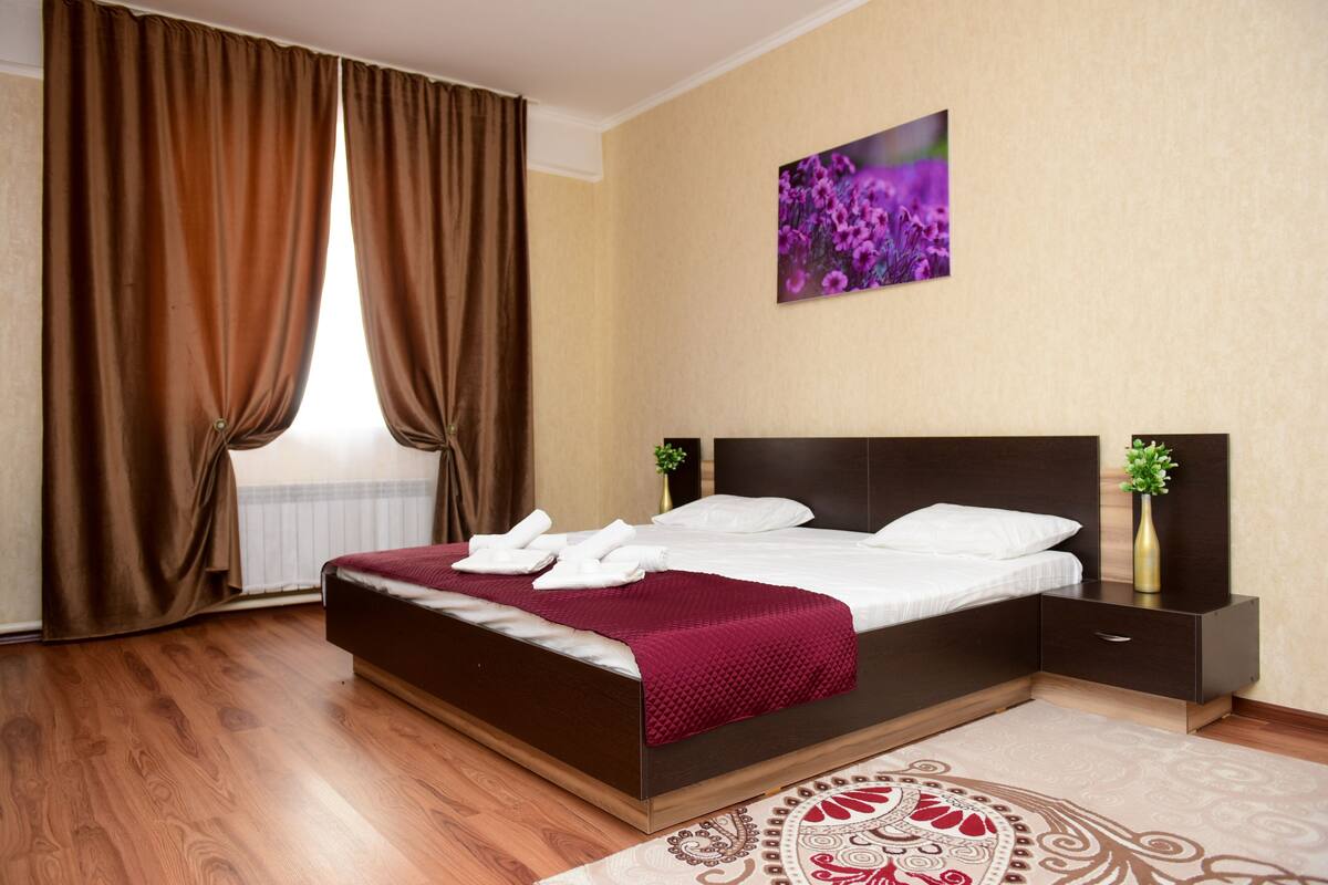 A hotel room with a large bed, a nightstand, a vase with a plant, and a painting on the wall.