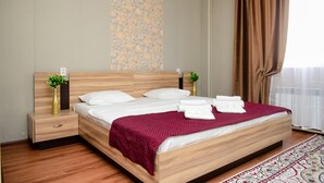 Ein ordentlich bezogenes Bett mit roter Decke, Holz-Kopfteil und zwei Nachttischen mit Vasen.