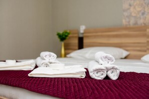 A neatly made bed with white towels and a red blanket, a wooden headboard, and a small plant in the background. - Alatau Hotel (Astana)