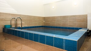 Ein rechteckiger Swimmingpool mit blauer Fliesenbordur, umgeben von braunen Fliesen, und zwei Metallleiter auf der linken Seite.