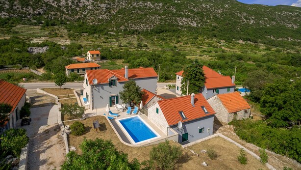 A residential area with houses, a swimming pool, and a mountainous backdrop. - Villa Roglic (Zagvozd)
