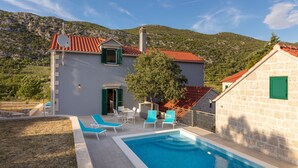 A two-story building with a swimming pool, outdoor seating, and a mountainous backdrop. - Villa Roglic (Zagvozd)