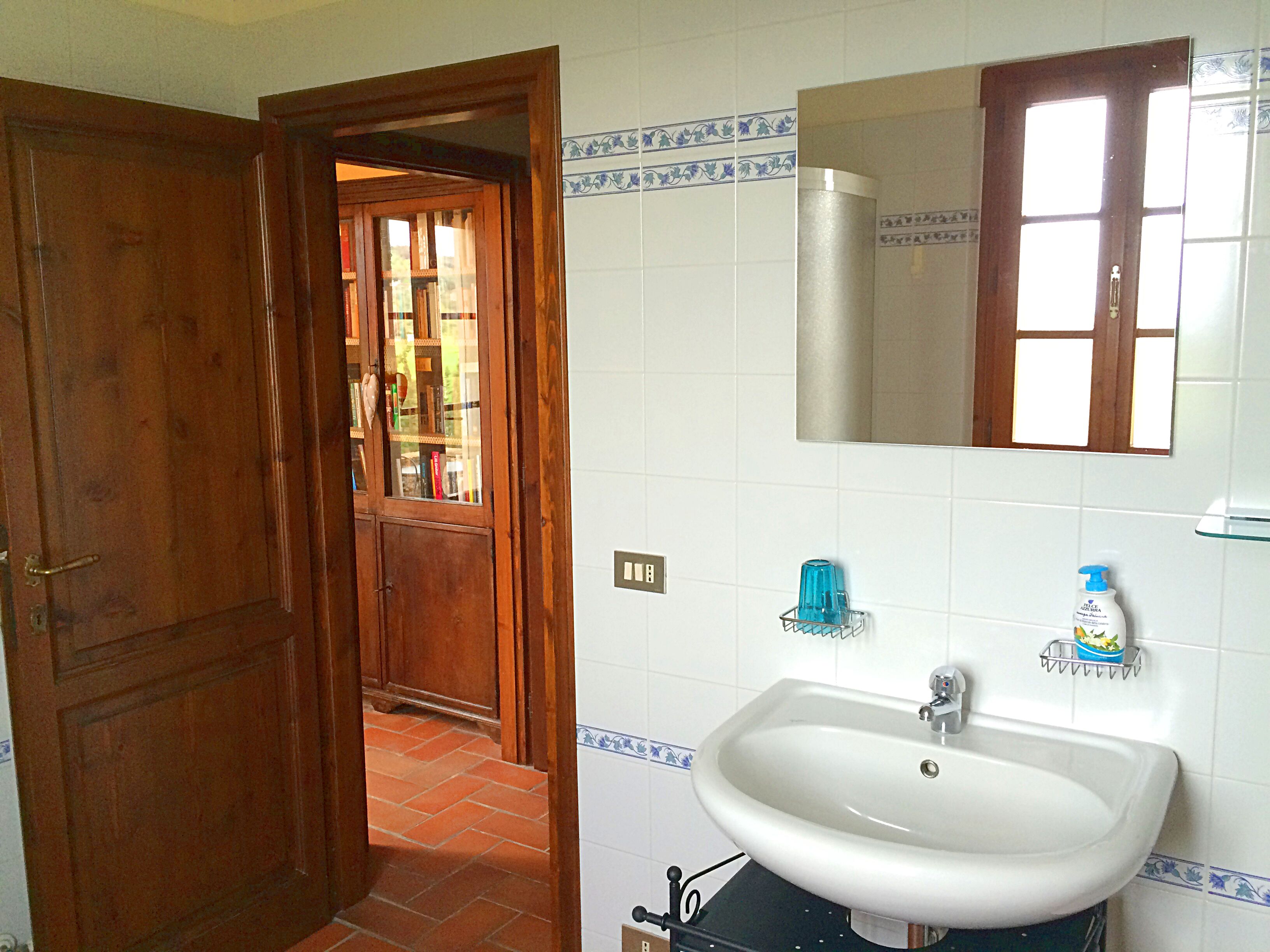 Un baño con un lavamanos blanco, un espejo encima y una ventana con marco de madera.