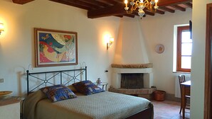 A bedroom with a bed, a fireplace, a painting, and a chandelier. - La Locanda del Barbagianni (Santa Luce)